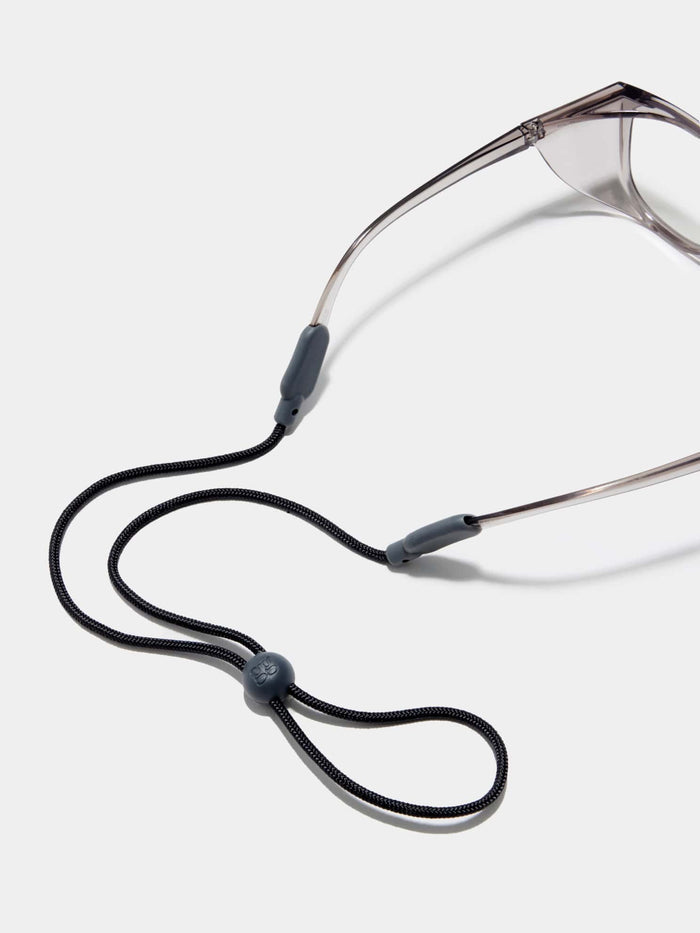 A shot of Stoggles sunglasses with a black neck cord resting on a white background, emphasizing functionality.